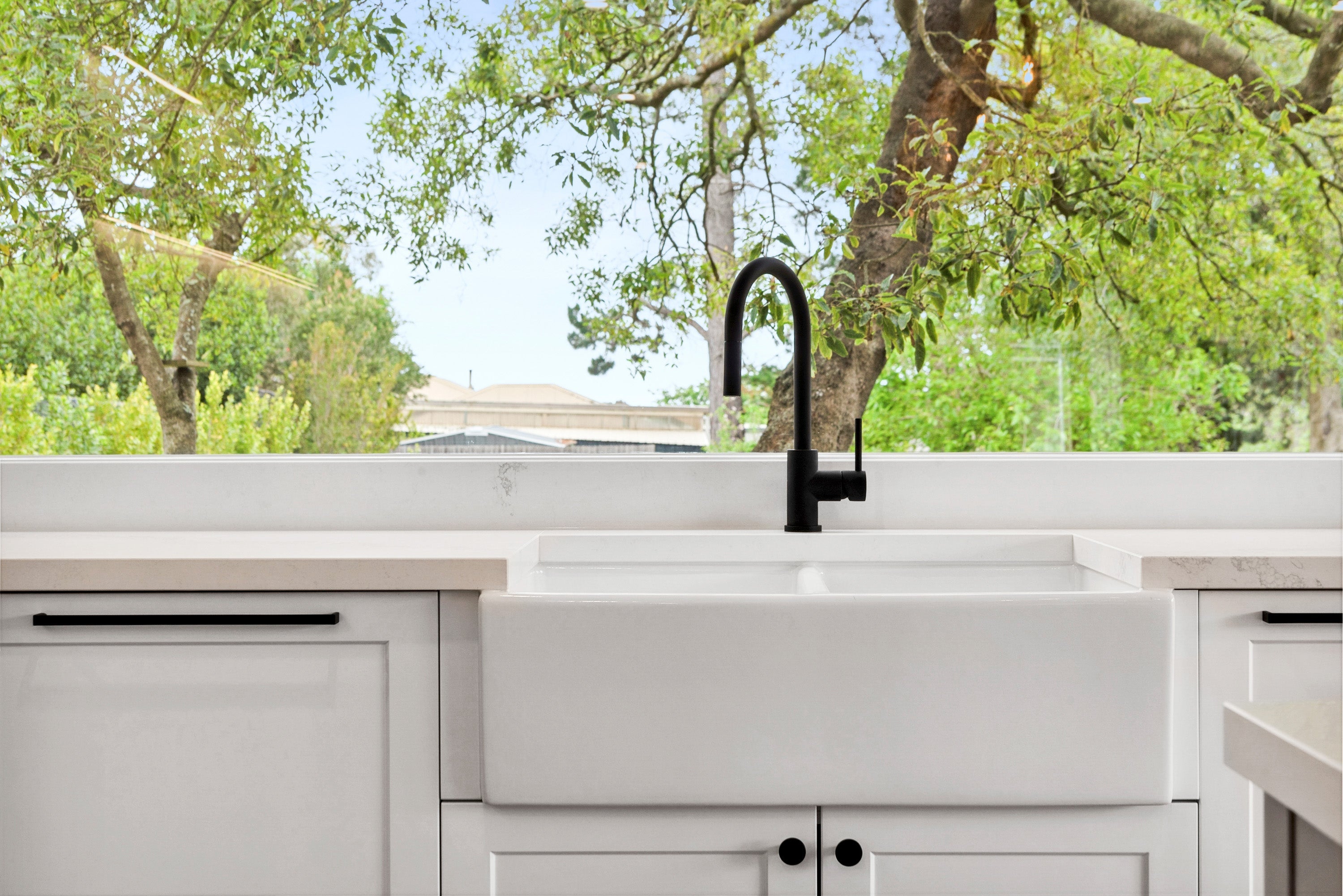 Matt Black kitchen tap with a white porcelain sink in front of big greenery filled glass window