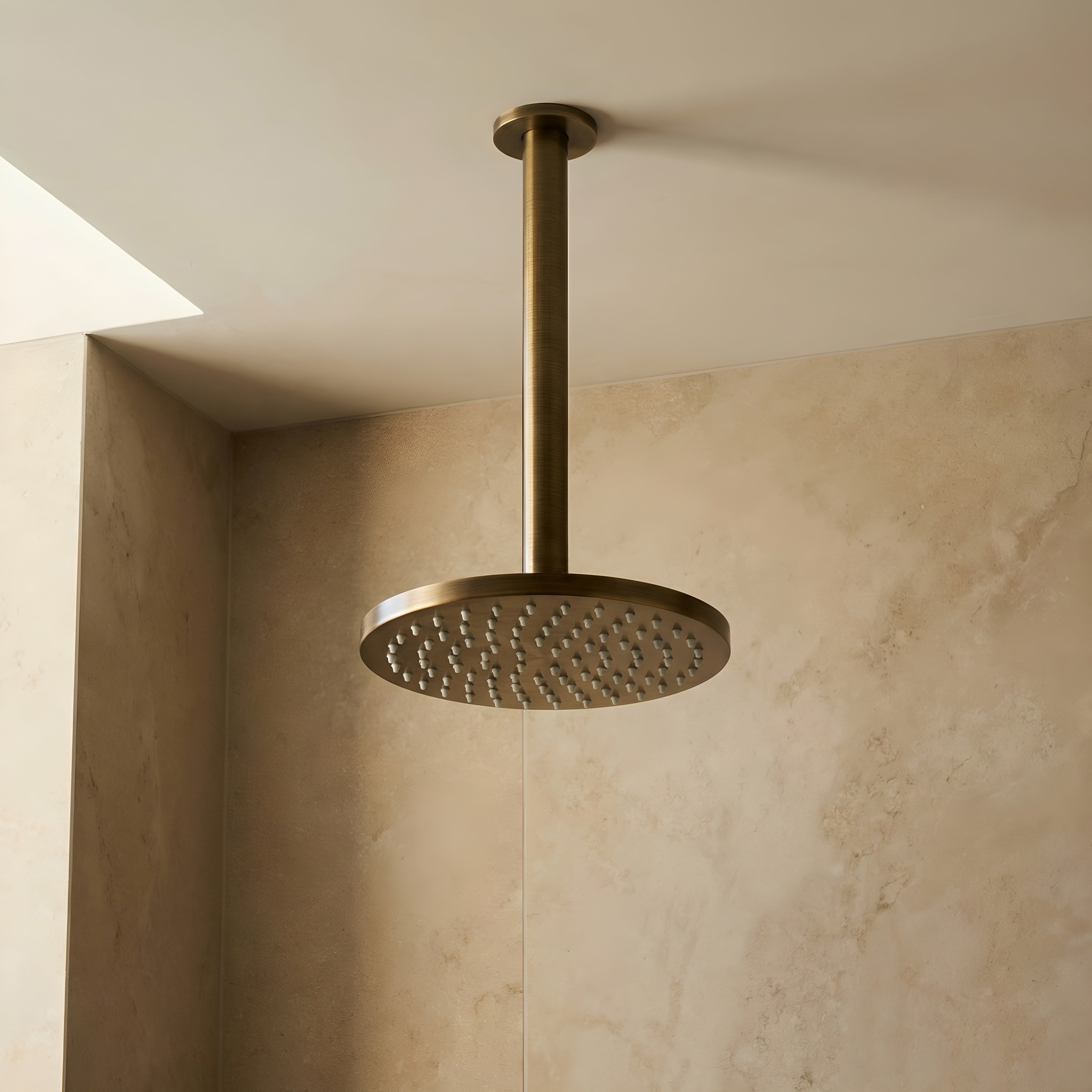 a brushed gold twin function shower with handheld wand on a grey tile background