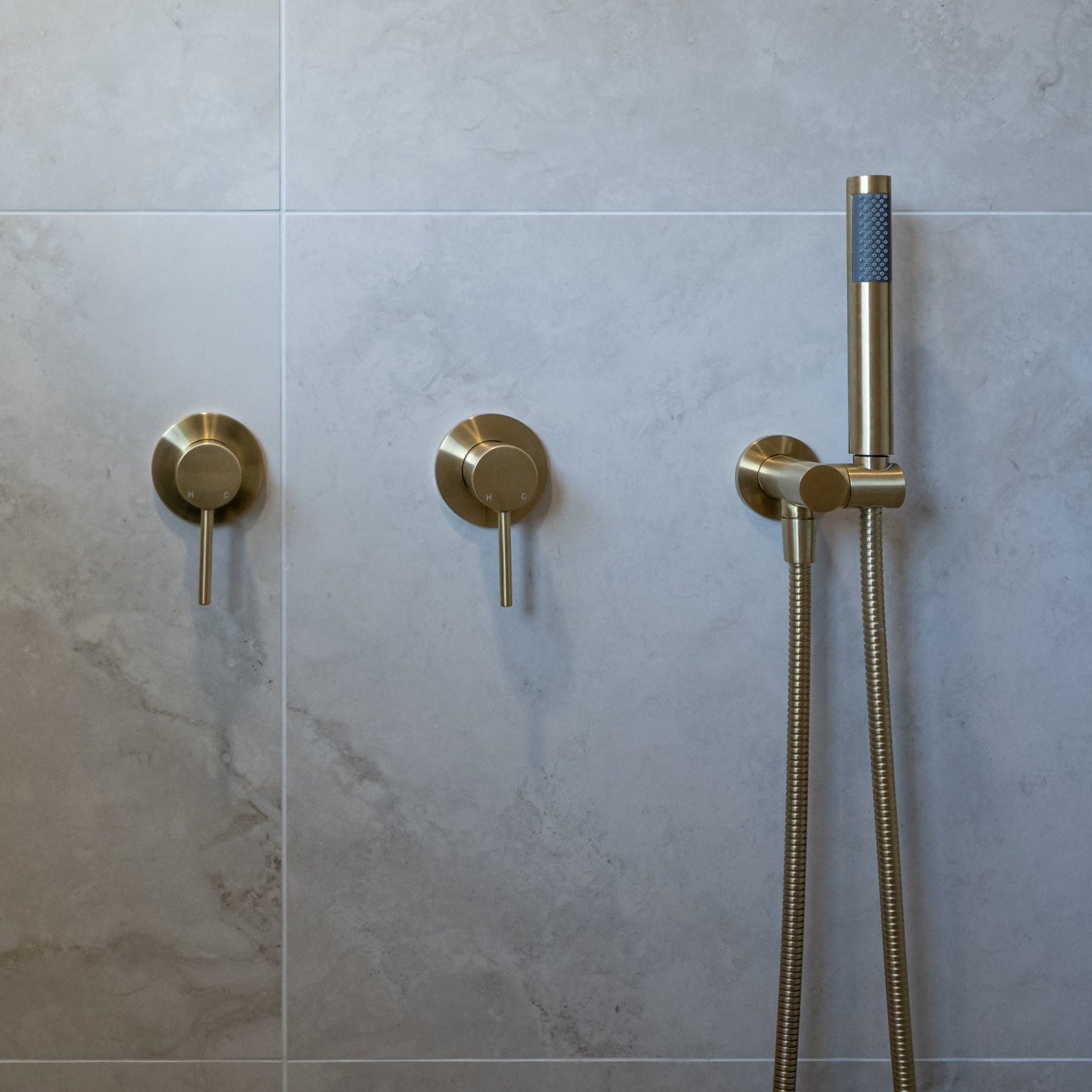 a brushed gold handheld shower piece on a wall mounted bracket on a grey tile in the shower