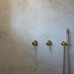 a brushed gold handheld shower piece on a wall mounted bracket on a grey tile in the shower