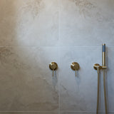 a brushed gold handheld shower piece on a wall mounted bracket on a grey tile in the shower