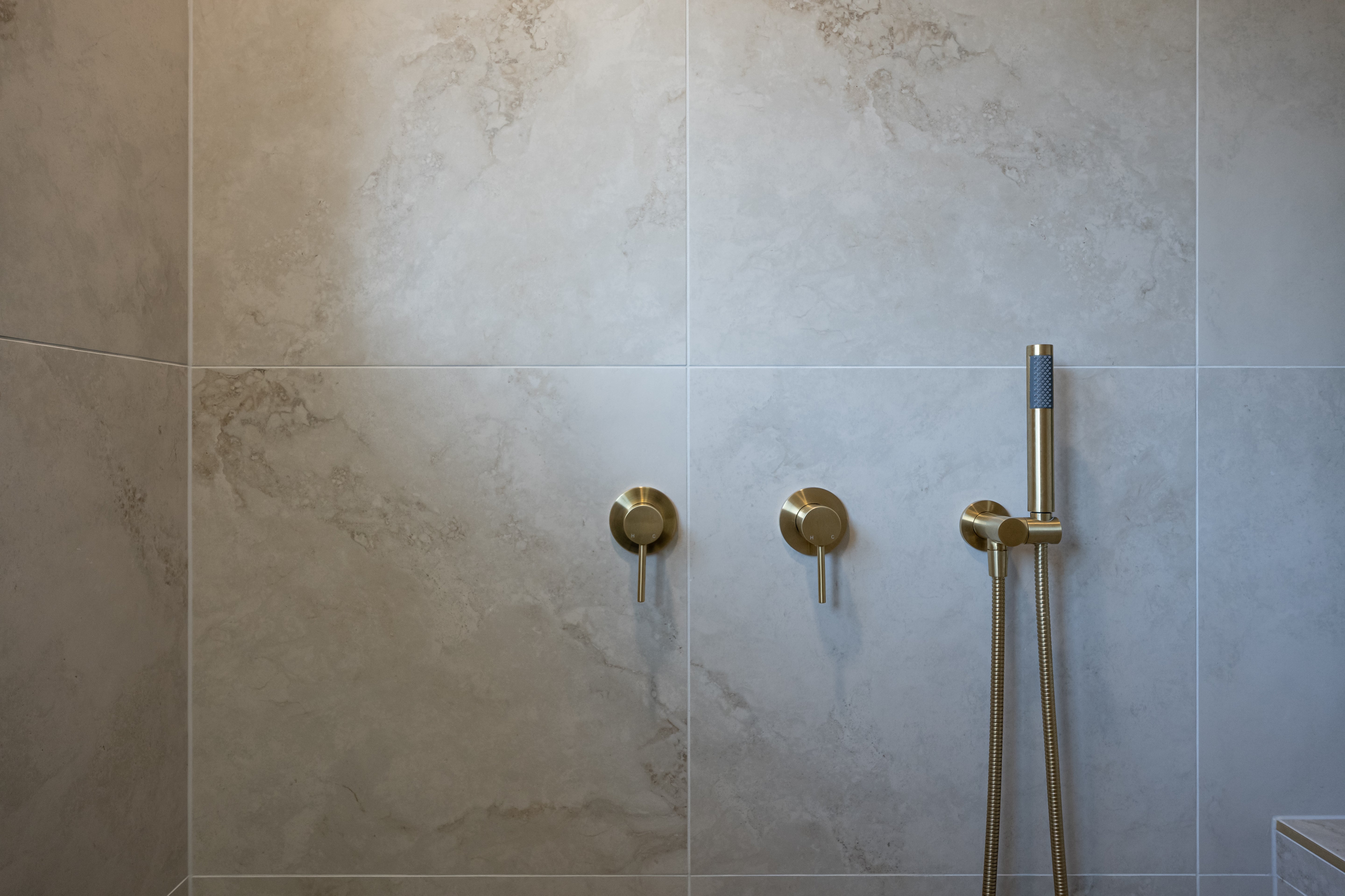 a brushed gold handheld shower piece on a wall mounted bracket on a grey tile in the shower