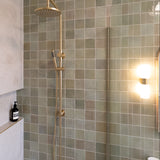 brushed gold twin round combination shower rail with diverter on a green feature tile background in a modern bathroom