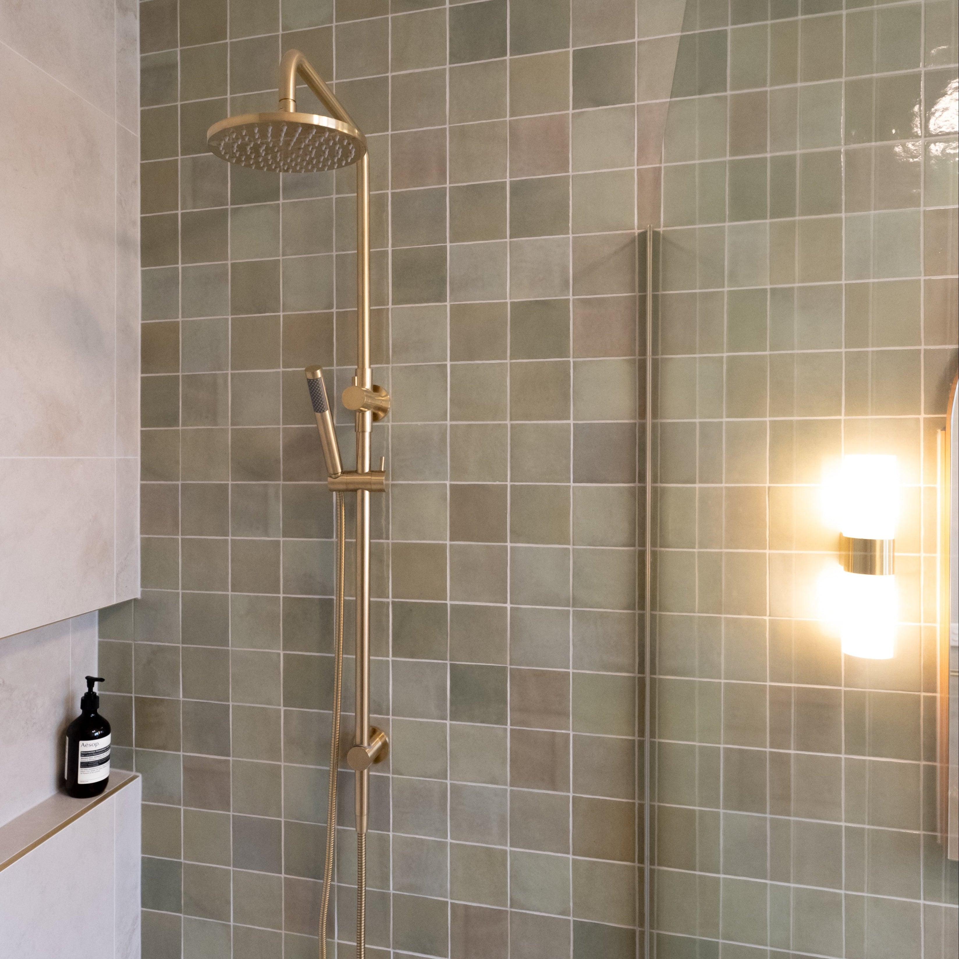 brushed gold twin round combination shower rail with diverter on a green feature tile background in a modern bathroom