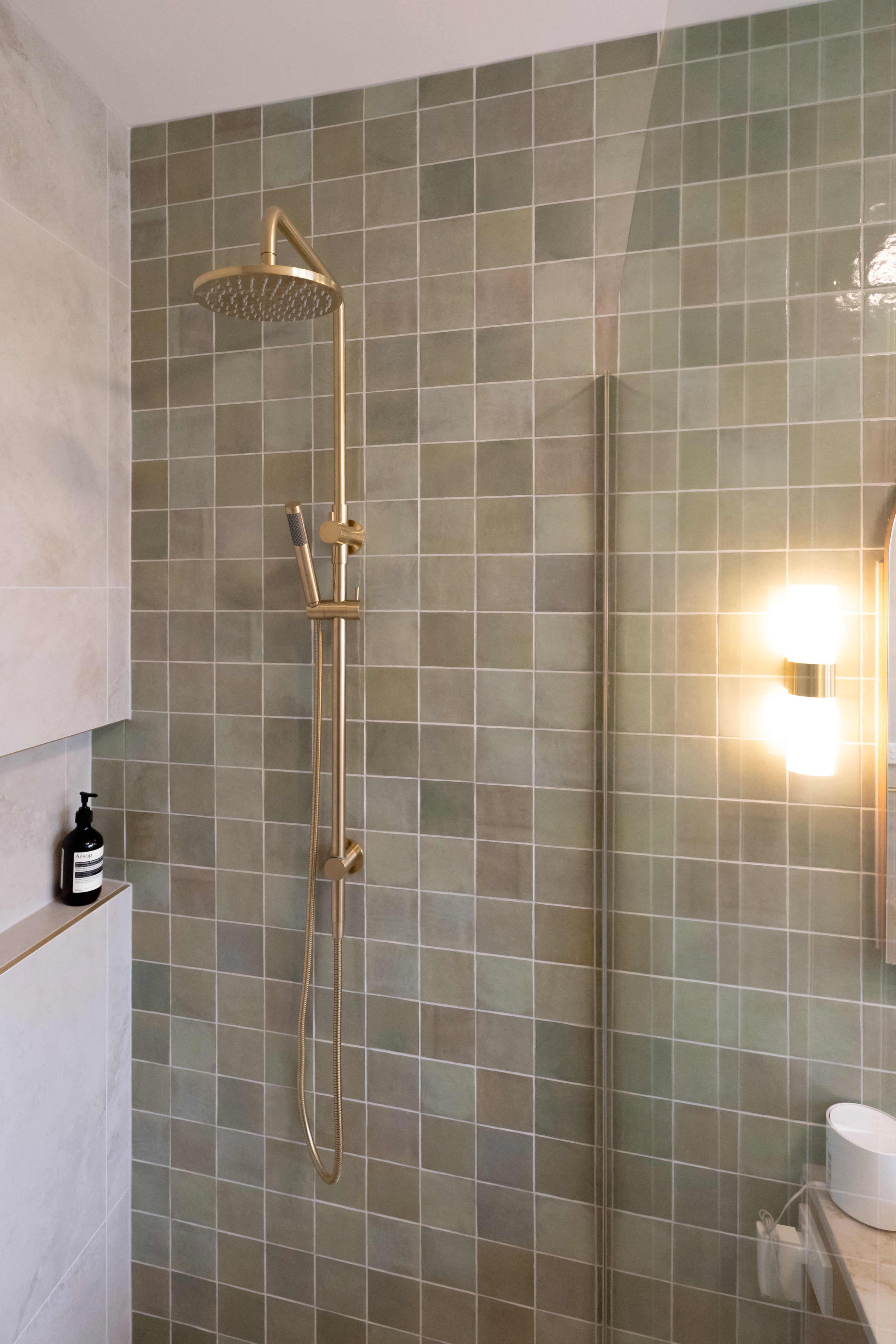brushed gold twin round combination shower rail with diverter on a green feature tile background in a modern bathroom