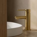 Brushed Gold basin mixer with round spout on a white sink against a neutral wall