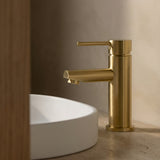 Brushed Gold basin mixer with round spout on a white sink against a neutral wall