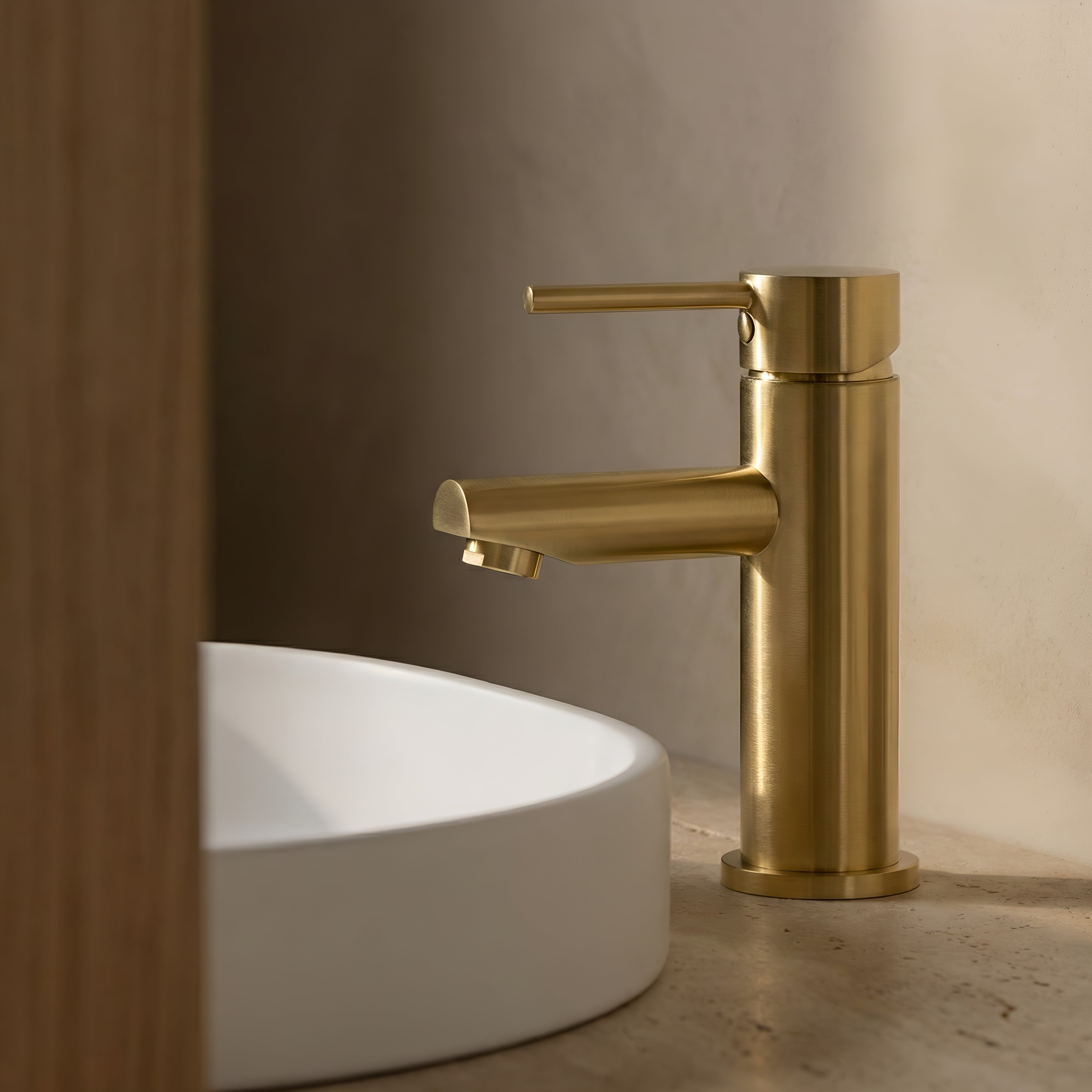 Brushed Gold basin mixer with round spout on a white sink against a neutral wall