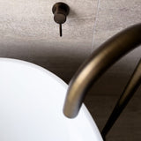 A close up photo of the antique brass floor spout with the wall mixer, showing the texture of the tapware and warmth of the colour.