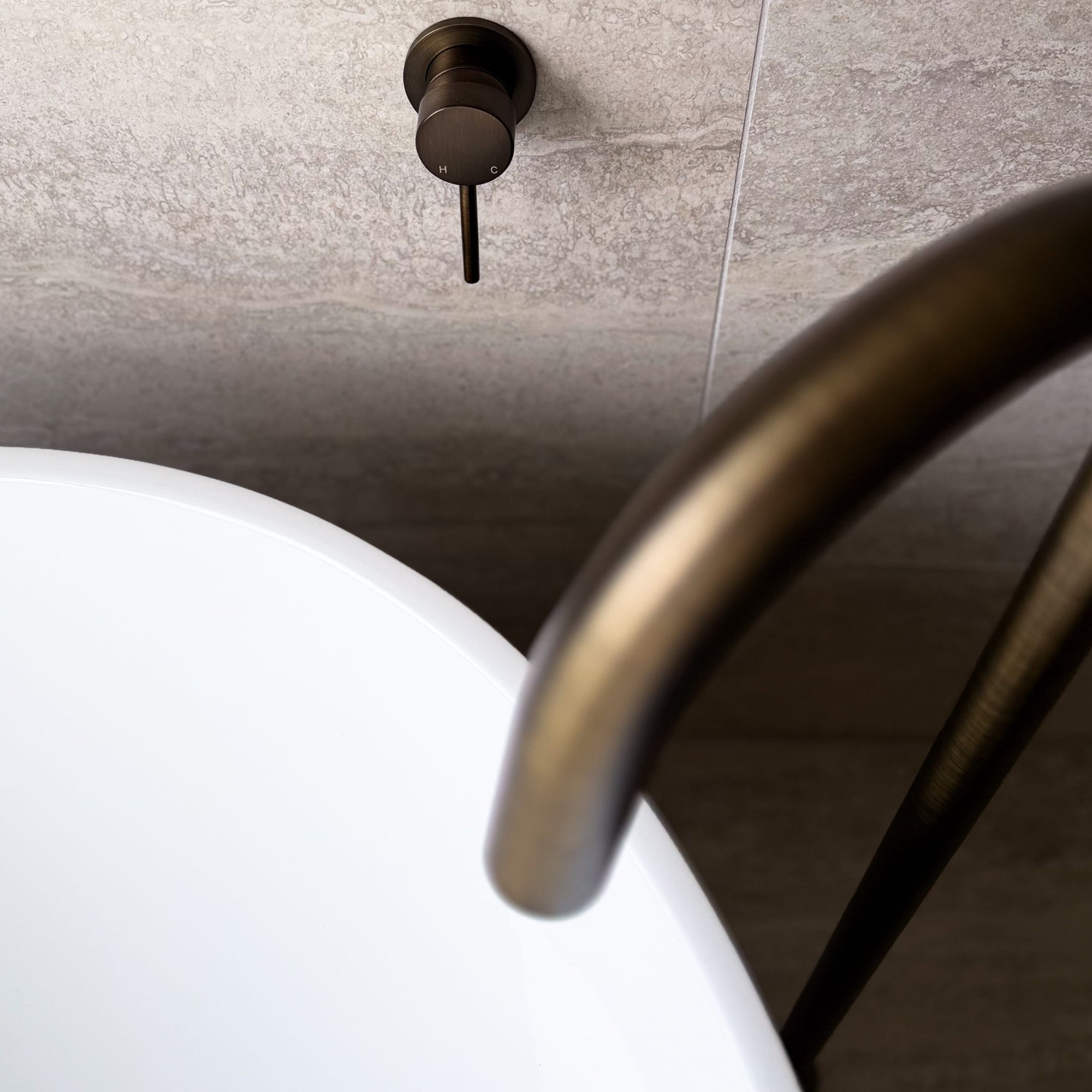 A close up photo of the antique brass floor spout with the wall mixer, showing the texture of the tapware and warmth of the colour.