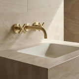 Brushed Gold cross handle taps with wall spout on a beige tiled wall with a white sink.