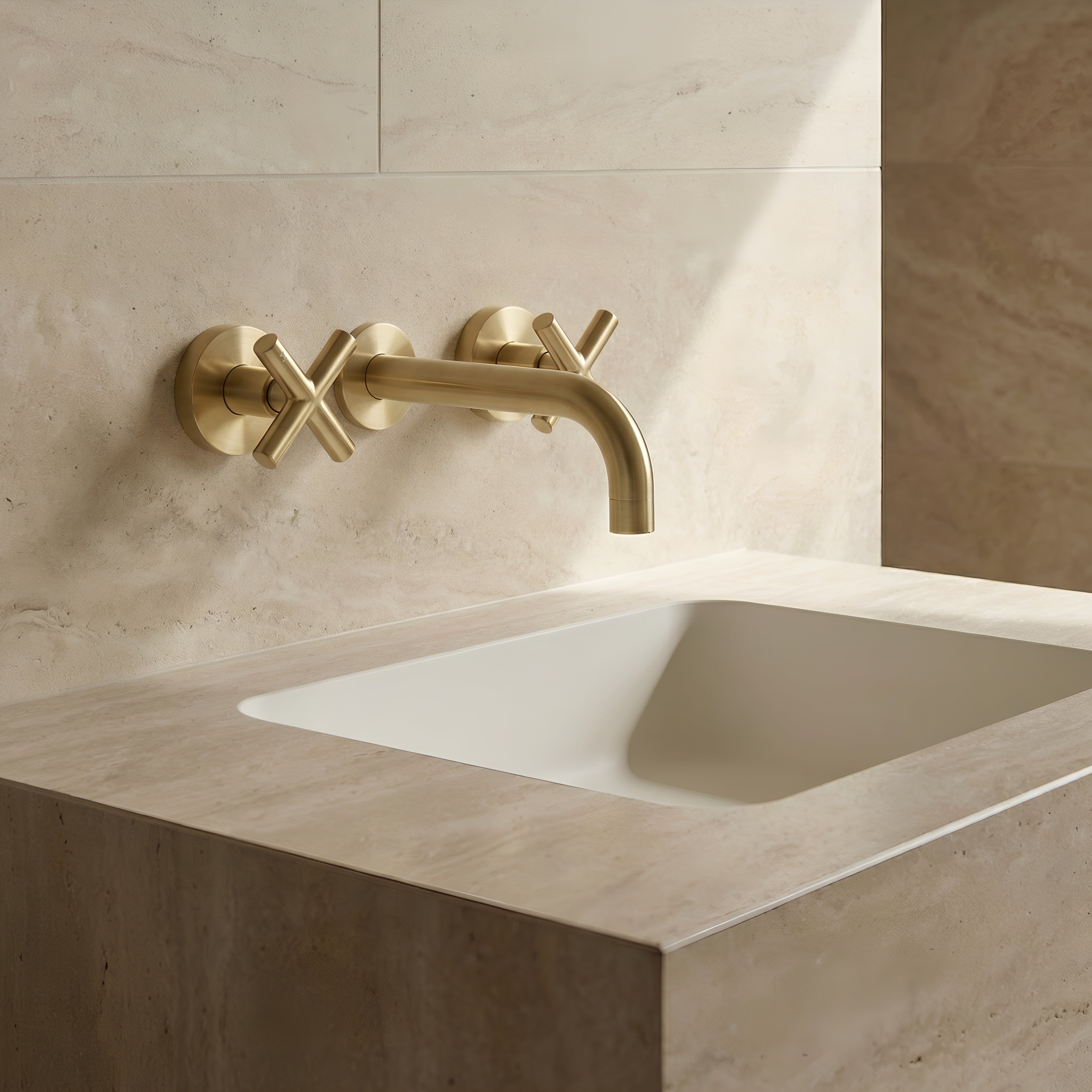 Brushed Gold cross handle taps with wall spout on a beige tiled wall with a white sink.