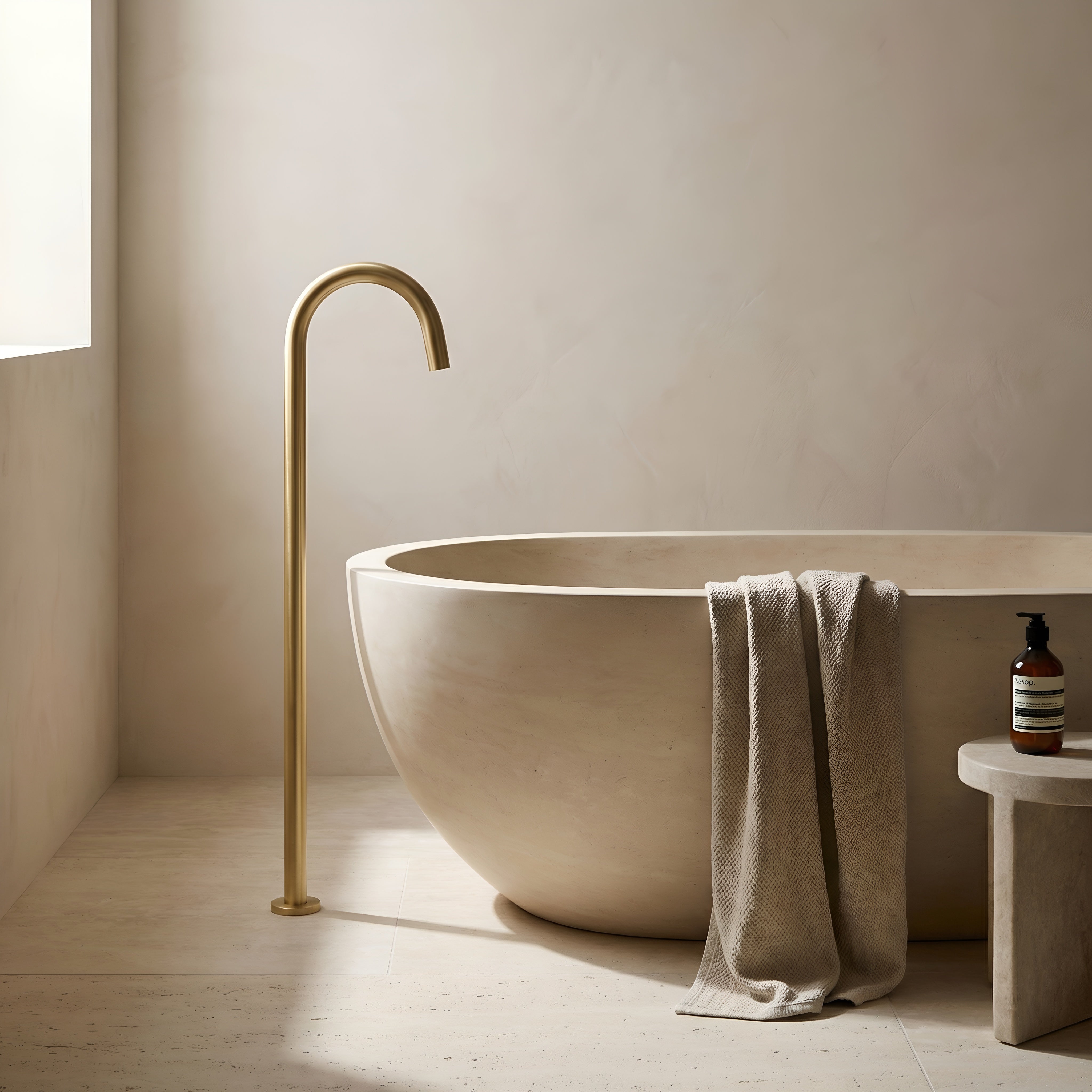 Beige freestanding bathtub with brushed gold floor spout in a minimalistic bathroom.