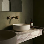 Bathroom vanity with a white sink, antique brass round wall taps and wall spout with a marble countertop.