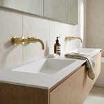 Modern bathroom sink with brushed gold round wall taps and wall spout on wooden cabinet.