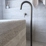 Modern antique brass floor bath spout in a bathroom setting with a towel and decorative items.