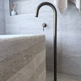 Modern antique brass floor bath spout in a bathroom setting with a towel and decorative items.