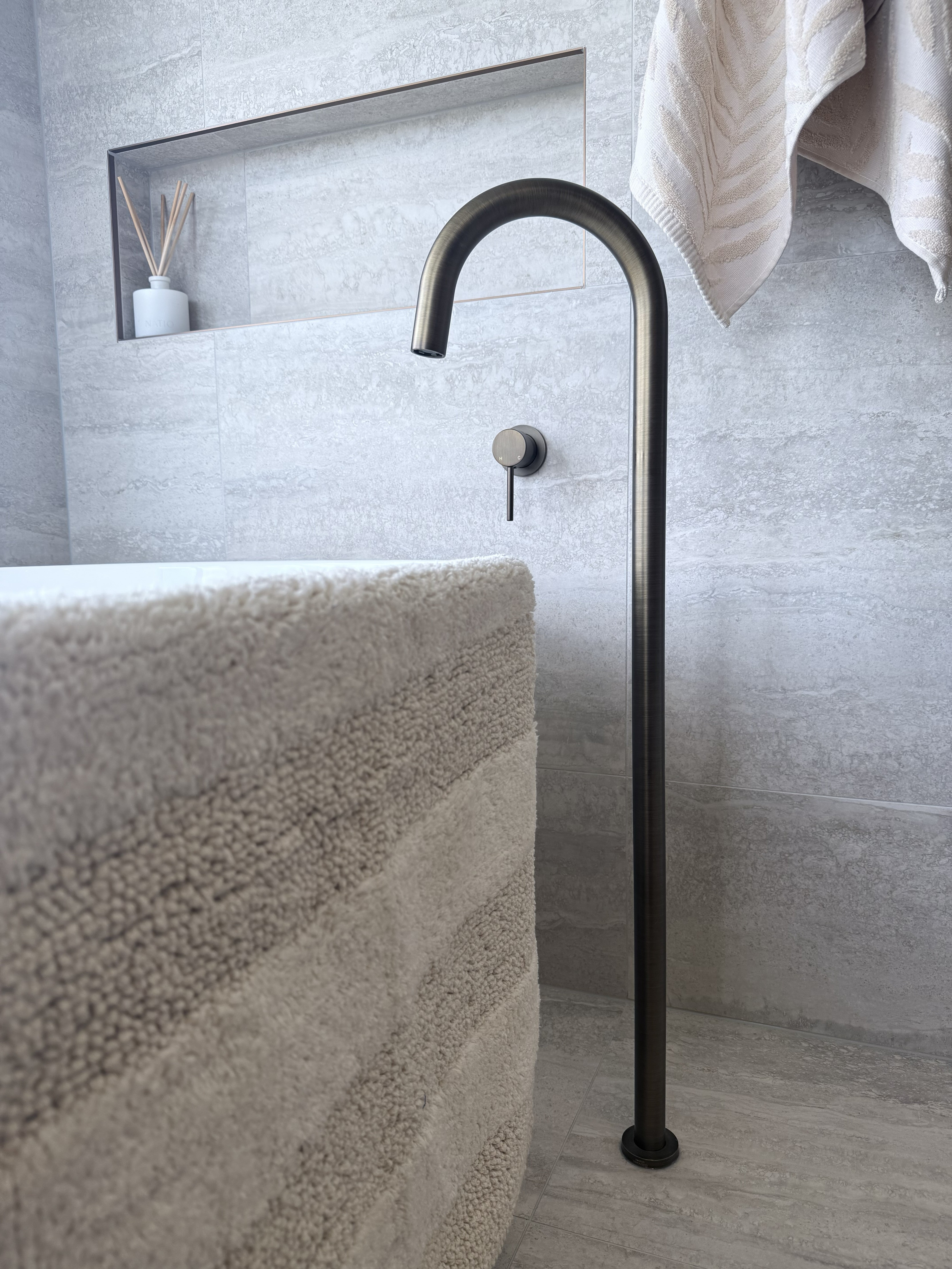 Modern antique brass floor bath spout in a bathroom setting with a towel and decorative items.