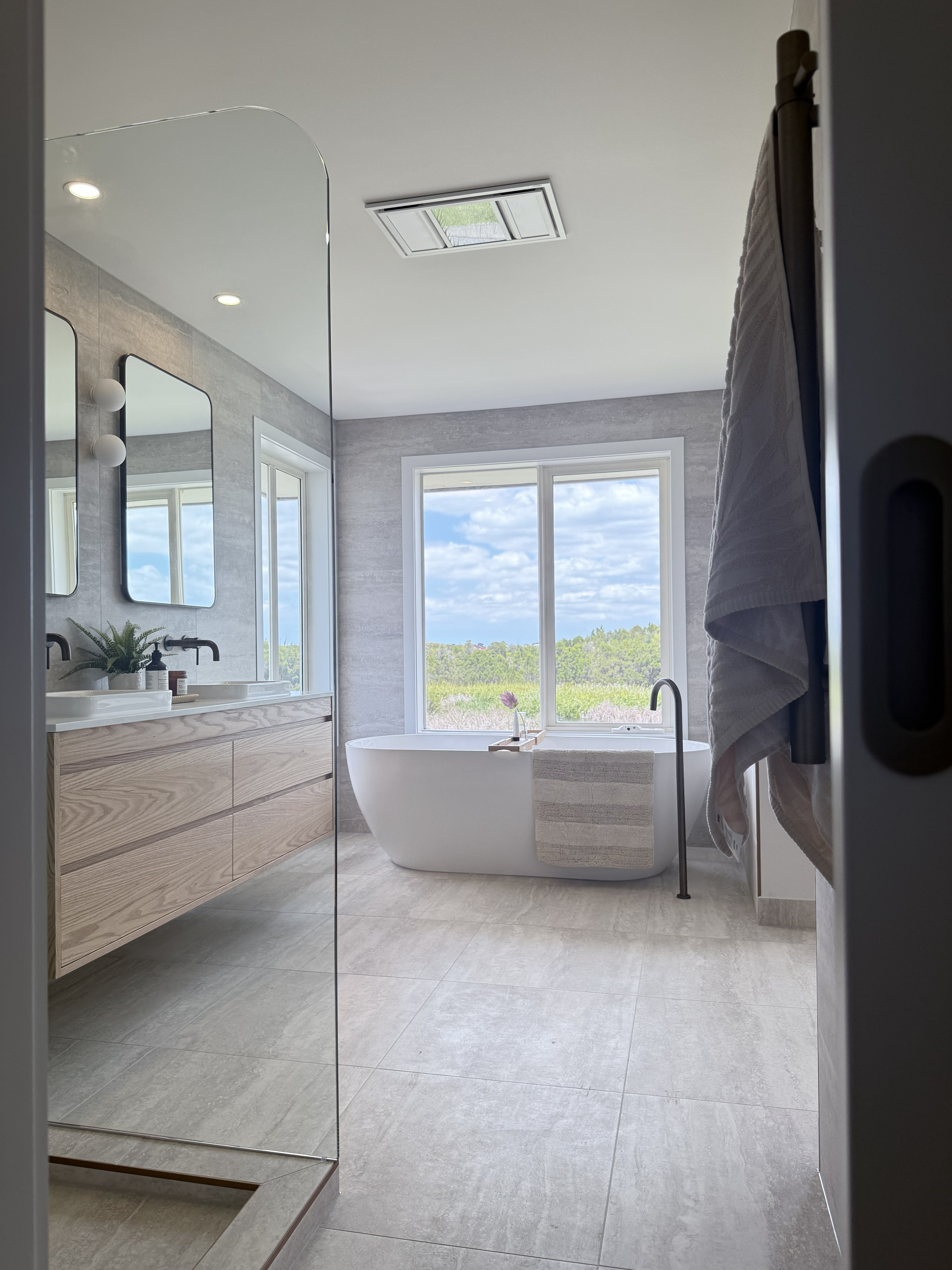 Modern bathroom with freestanding bathtub, large mirror, and window view