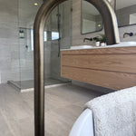Bathroom interior with a freestanding bathtub, wooden vanity, antique brass floor spout and glass shower enclosure.