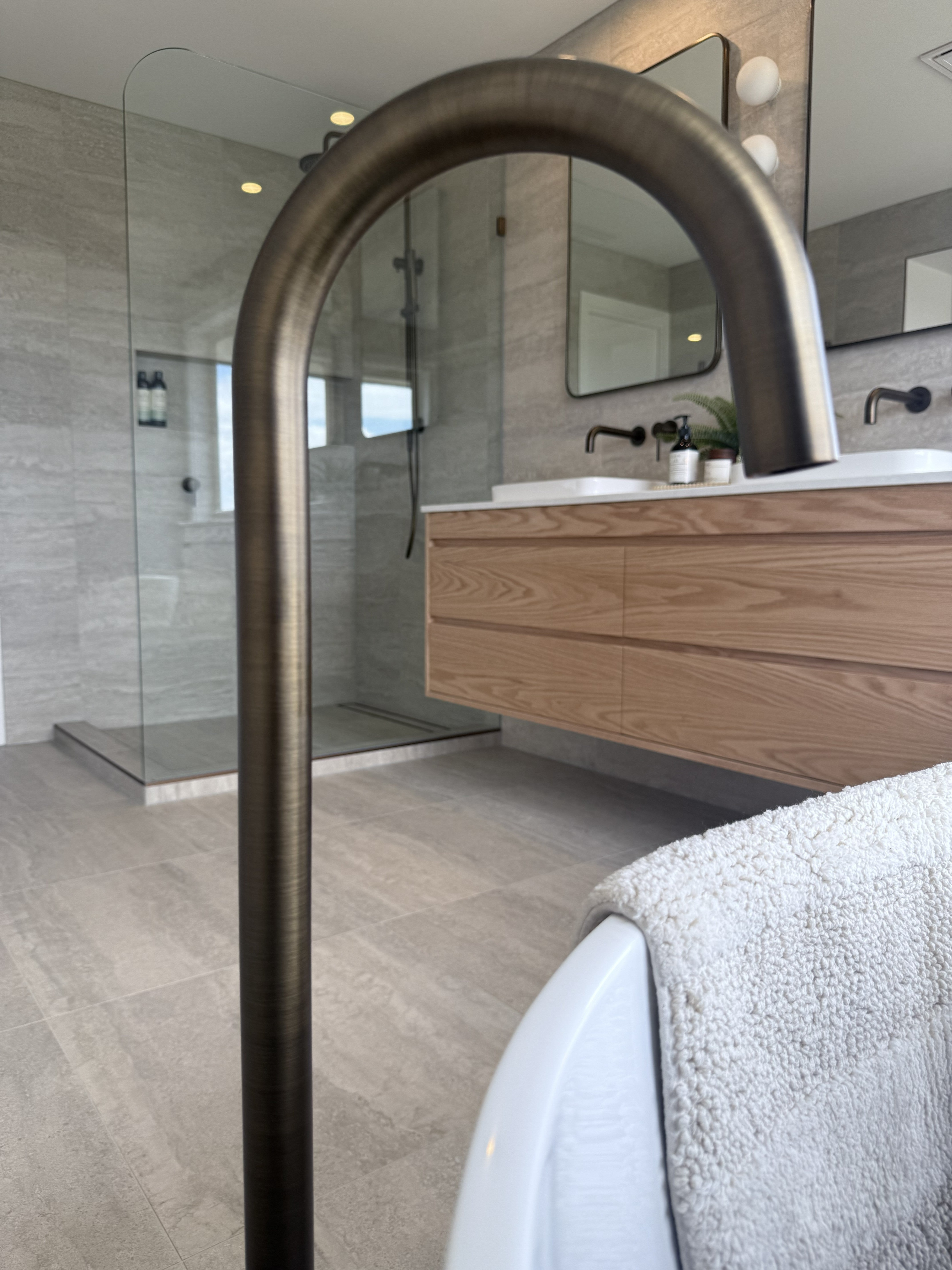 Bathroom interior with a freestanding bathtub, wooden vanity, antique brass floor spout and glass shower enclosure.