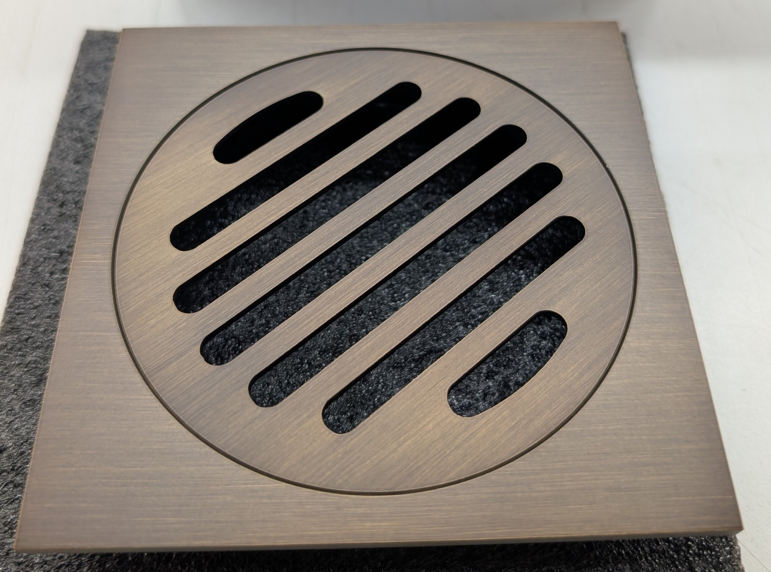 Antique brass floor grate cover with slotted design on a textured surface