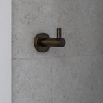 Antique brass robe hook on a grey tiled wall