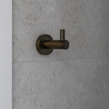 Antique brass robe hook on a grey tiled wall