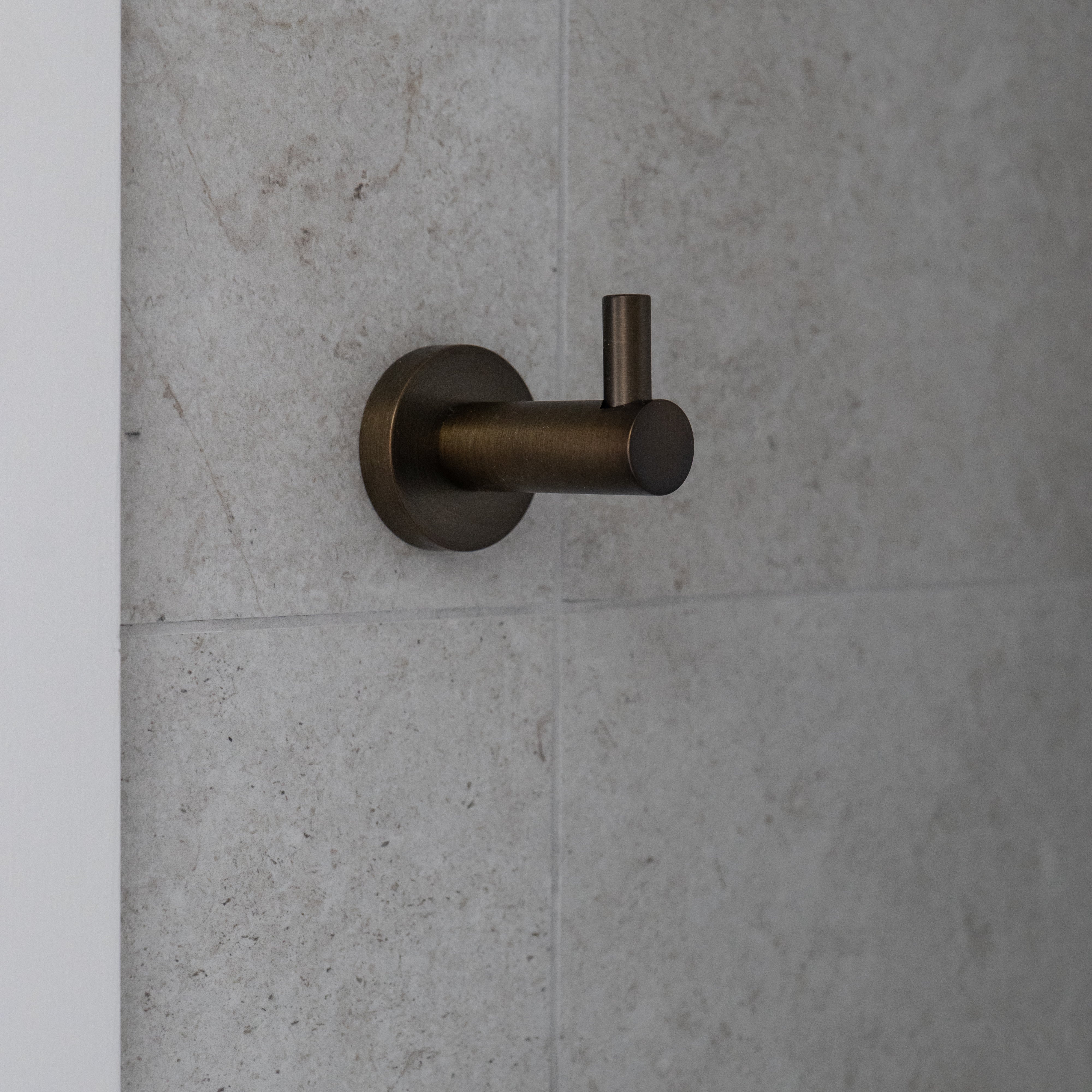 Antique brass robe hook on a grey tiled wall