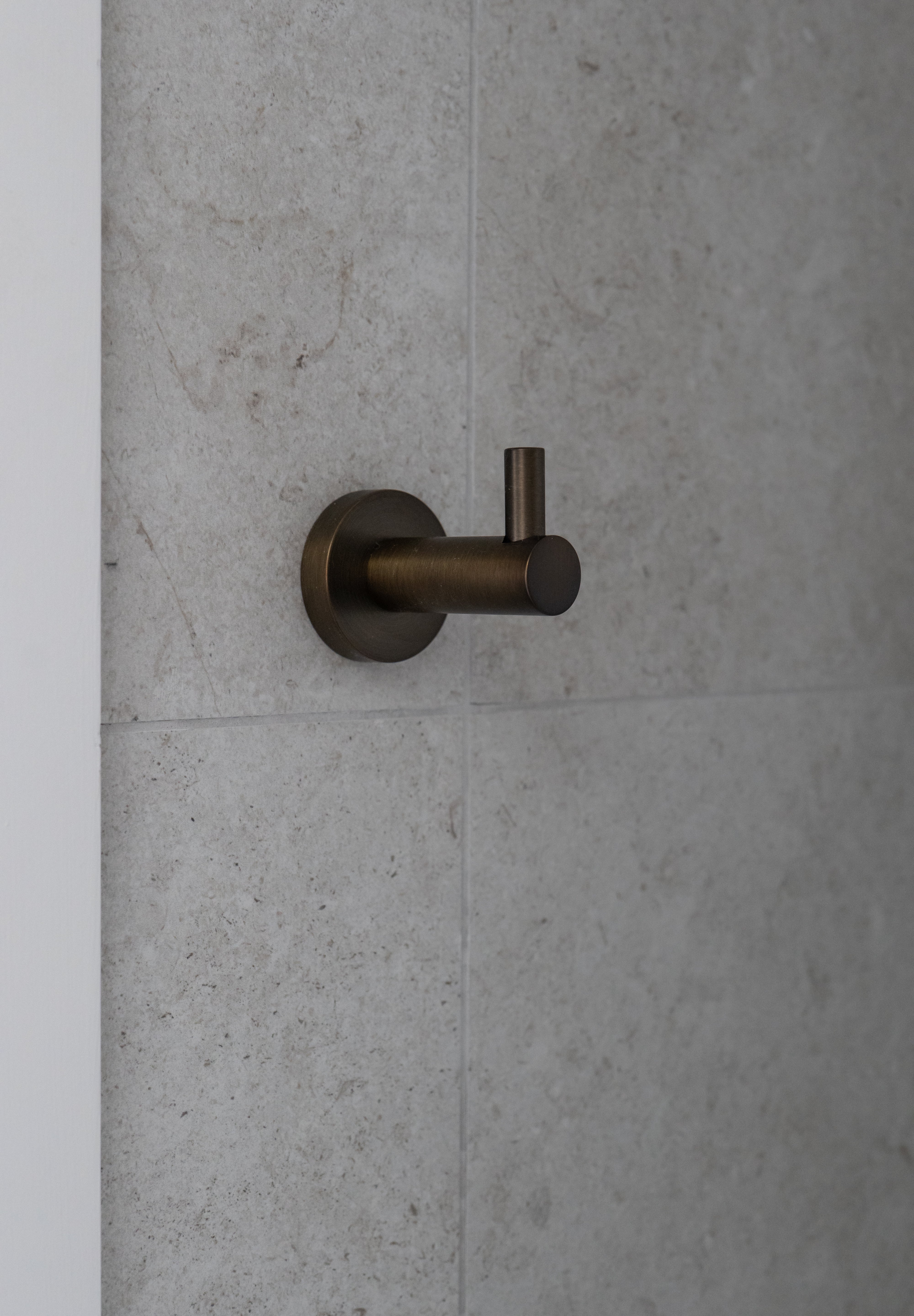 Antique brass robe hook on a grey tiled wall