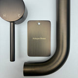 Antique brass bathroom fixtures including a sample disc, wall mixer and wall spout  on a grey background.