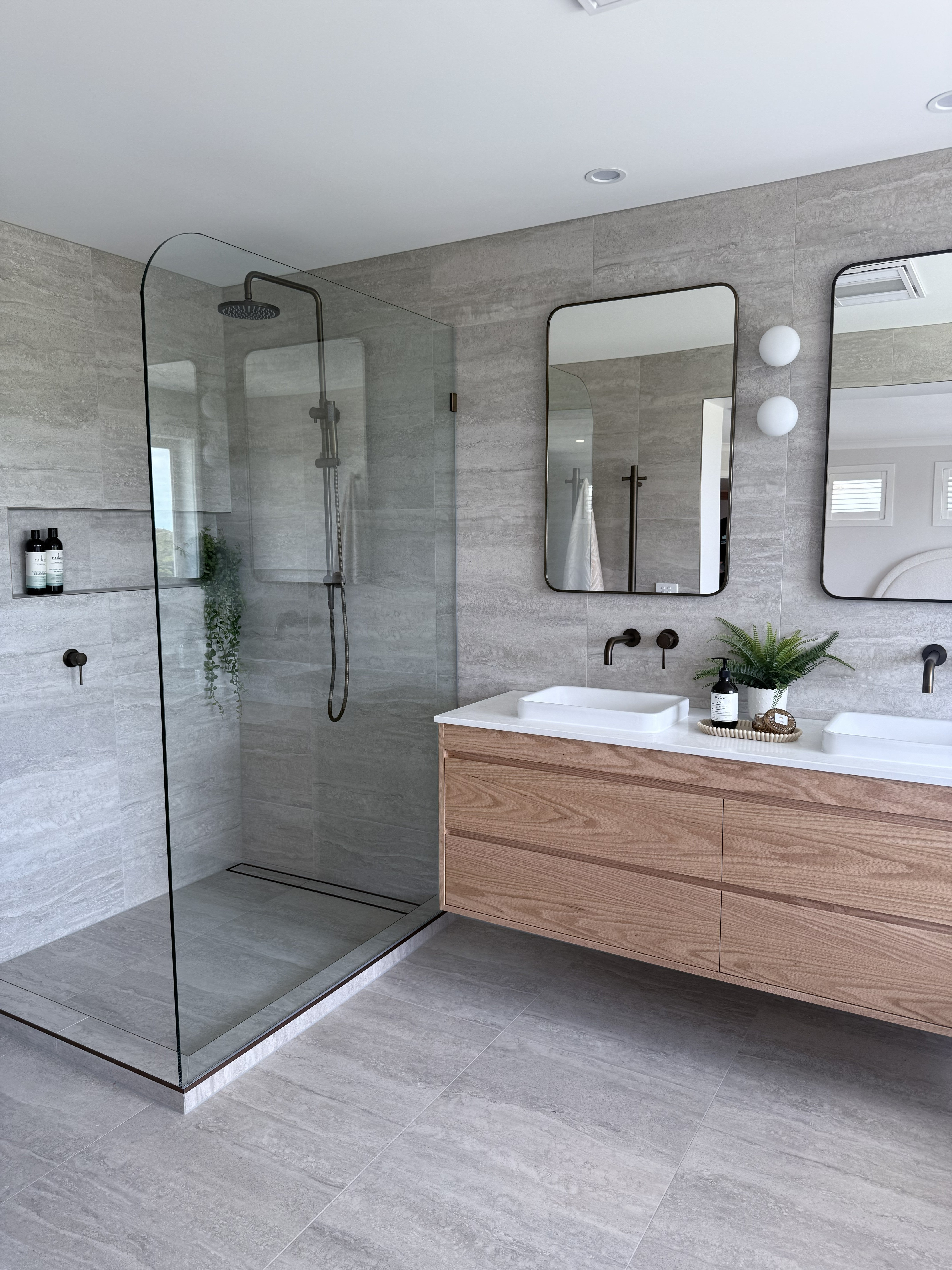 Antique Brass tapware in a modern bathroom with glass shower enclosure, wooden vanity, and large mirror.