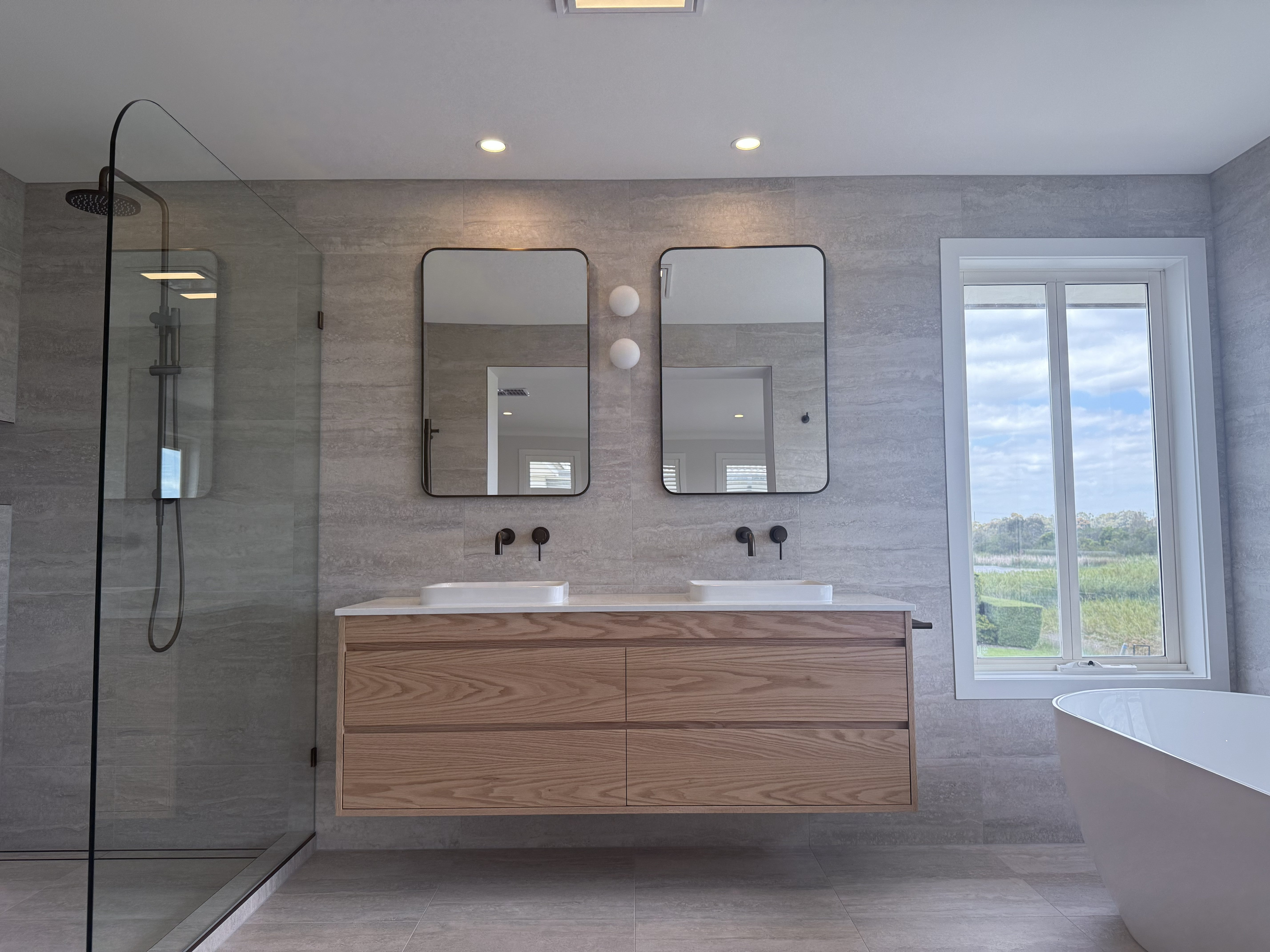 Modern bathroom with wooden vanity, mirrors, and a bathtub.