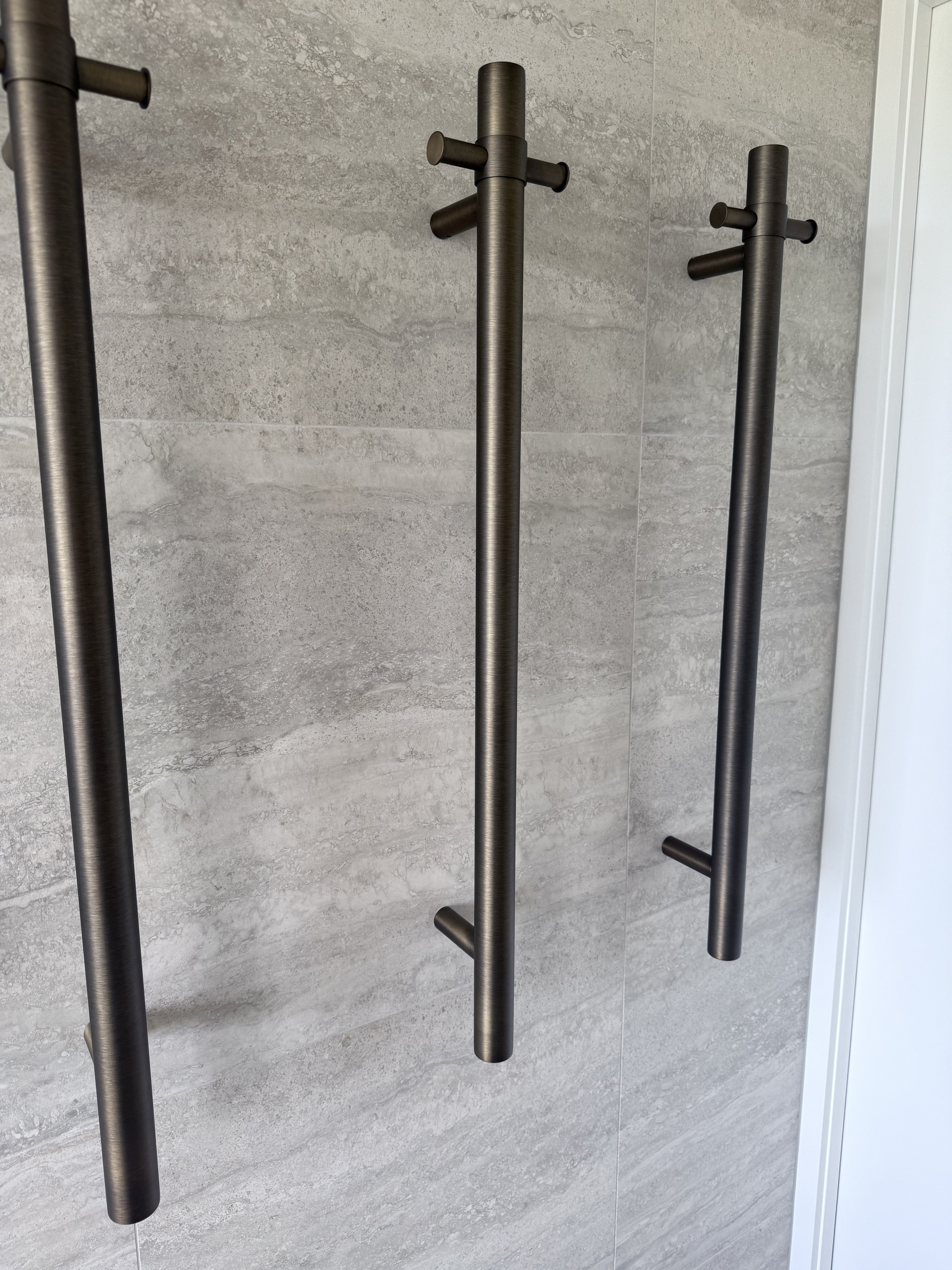 Set of antique brass single bar heated towel rails on a grey tiled wall