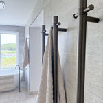 Bathroom with antique brass single bar heated towel rails and beige towels on a light grey tiled wall.
