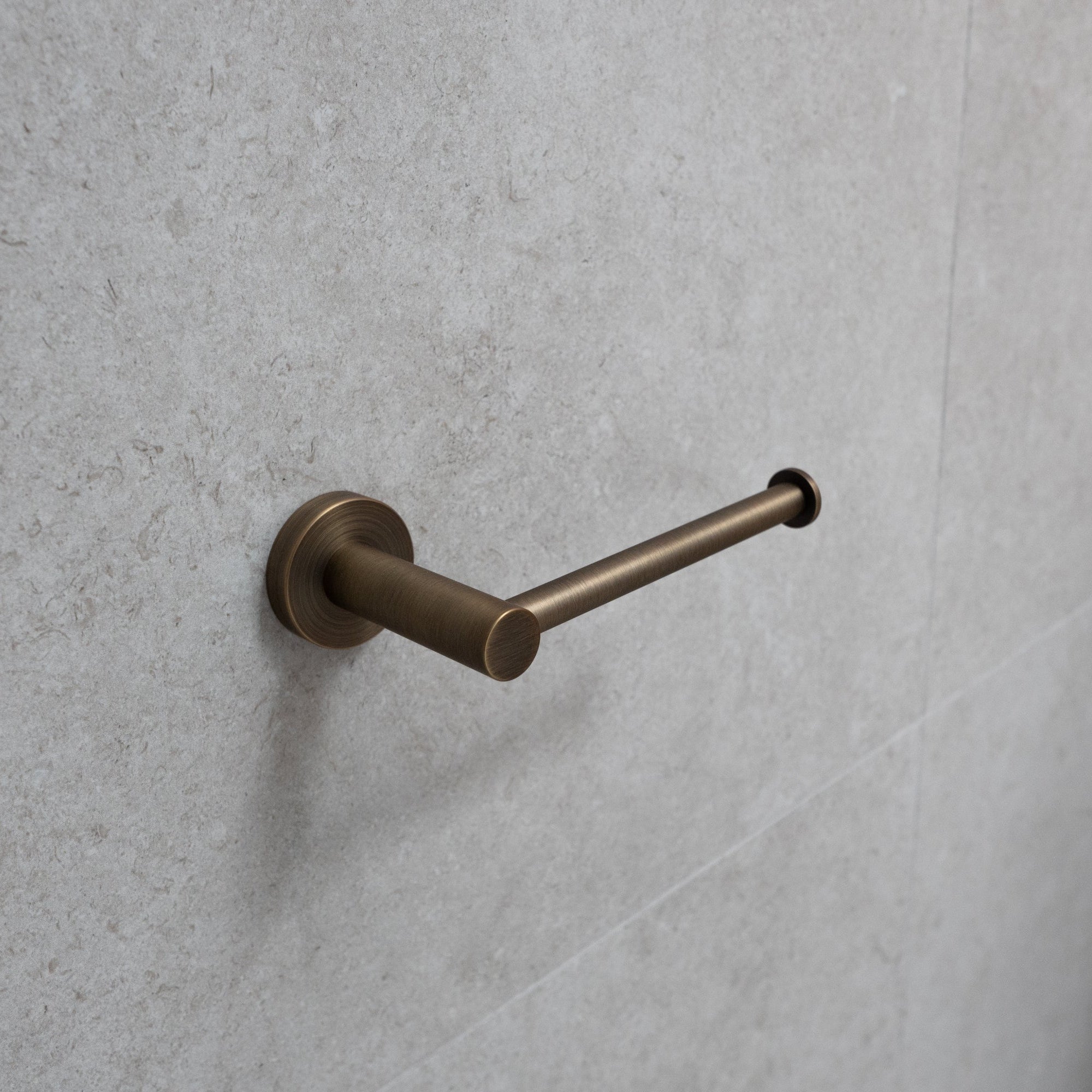 antique brass toilet roll holder on a grey tile background