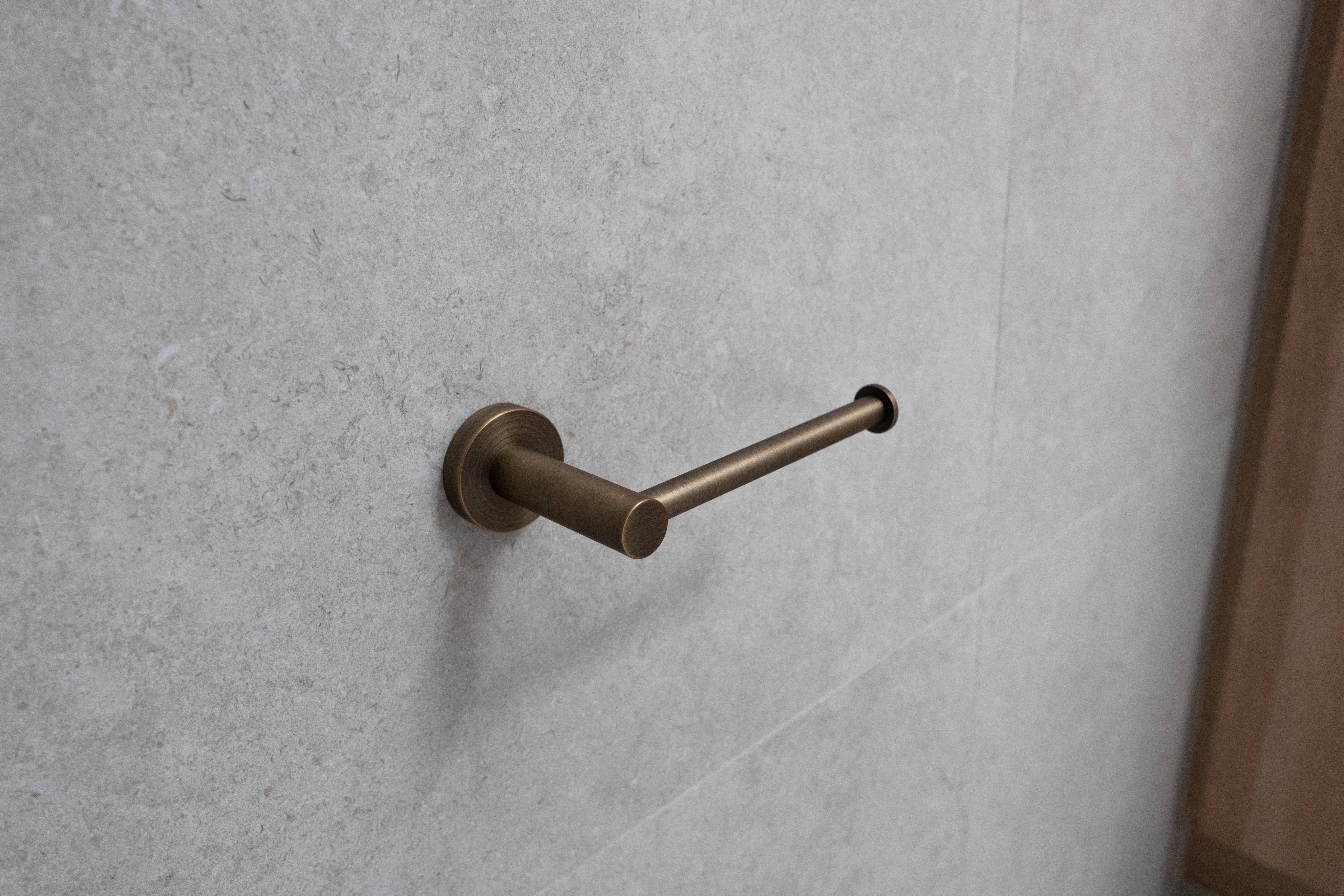 antique brass toilet roll holder on a grey tile background