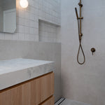 Antique Brass Twin Round Combination Shower Rail with Diverter and Hand Held wand on a grey tile background