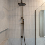 Antique brass shower head and hose mounted on a tiled wall in a bathroom.