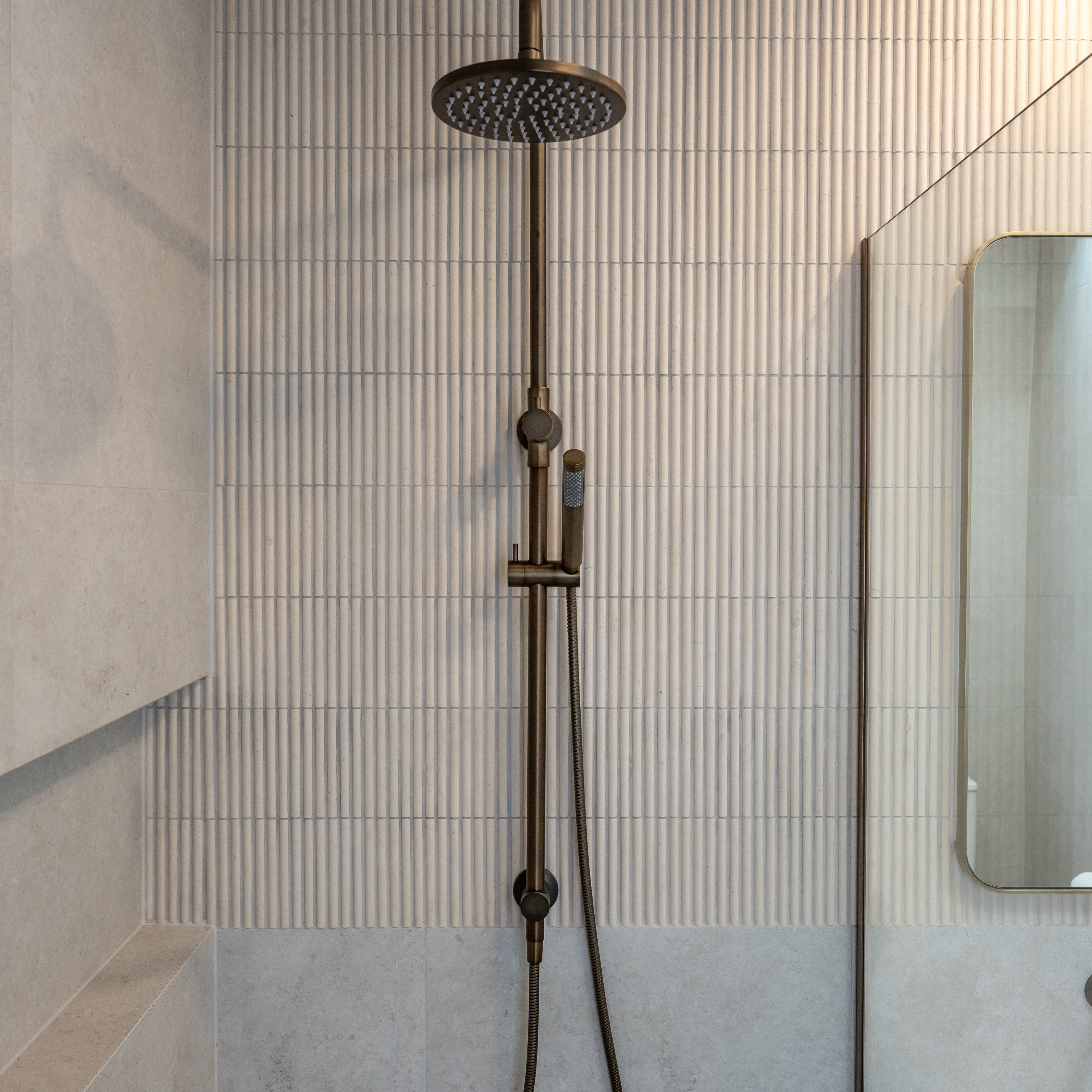 Antique brass shower head and hose mounted on a tiled wall in a bathroom.