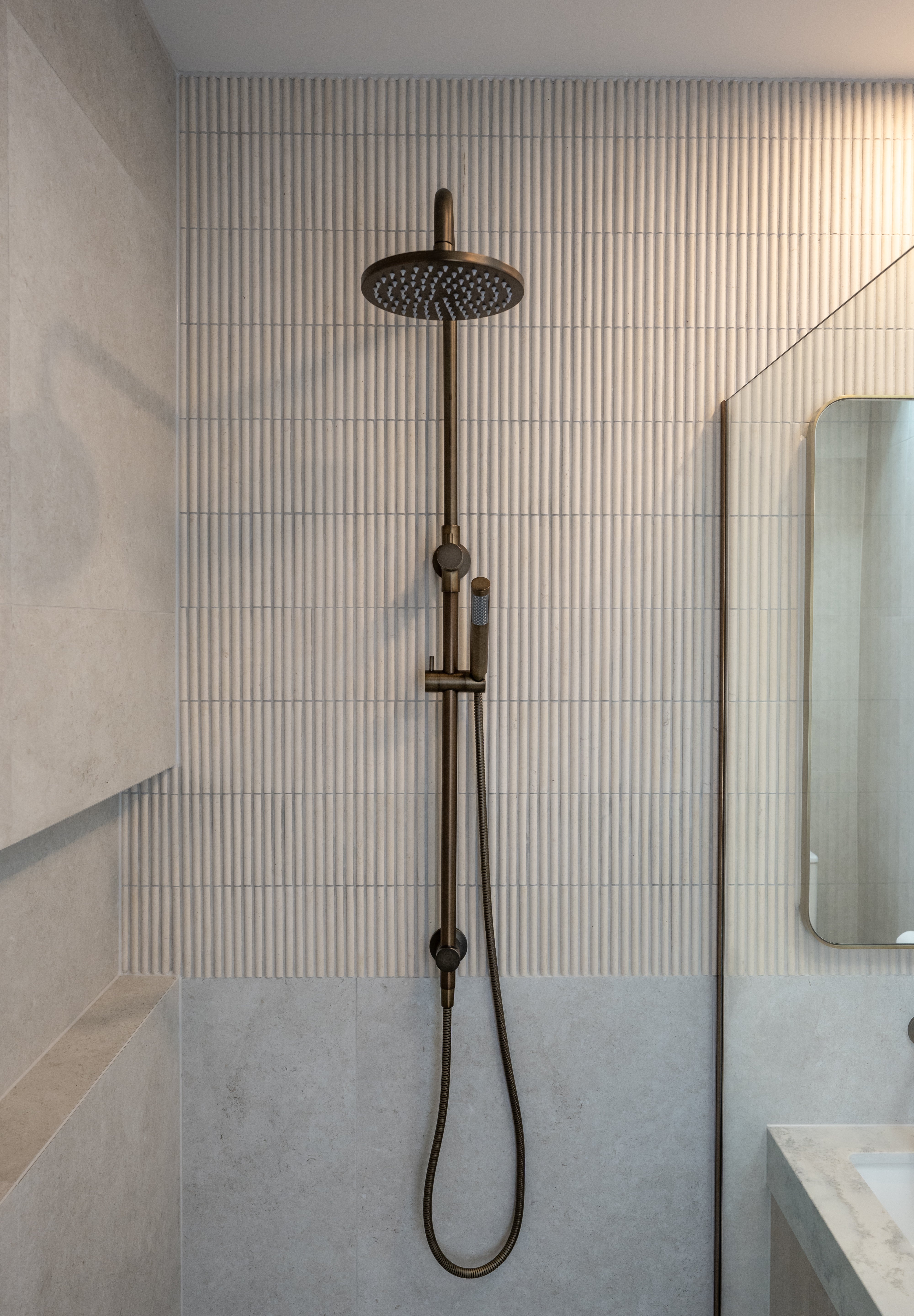 Antique brass shower head and hose mounted on a tiled wall in a bathroom.