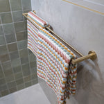 Brushed gold towel rail with a colorful striped towel against a tiled bathroom wall.