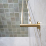 A brushed gold double towel rail wall mounted on a tile wall