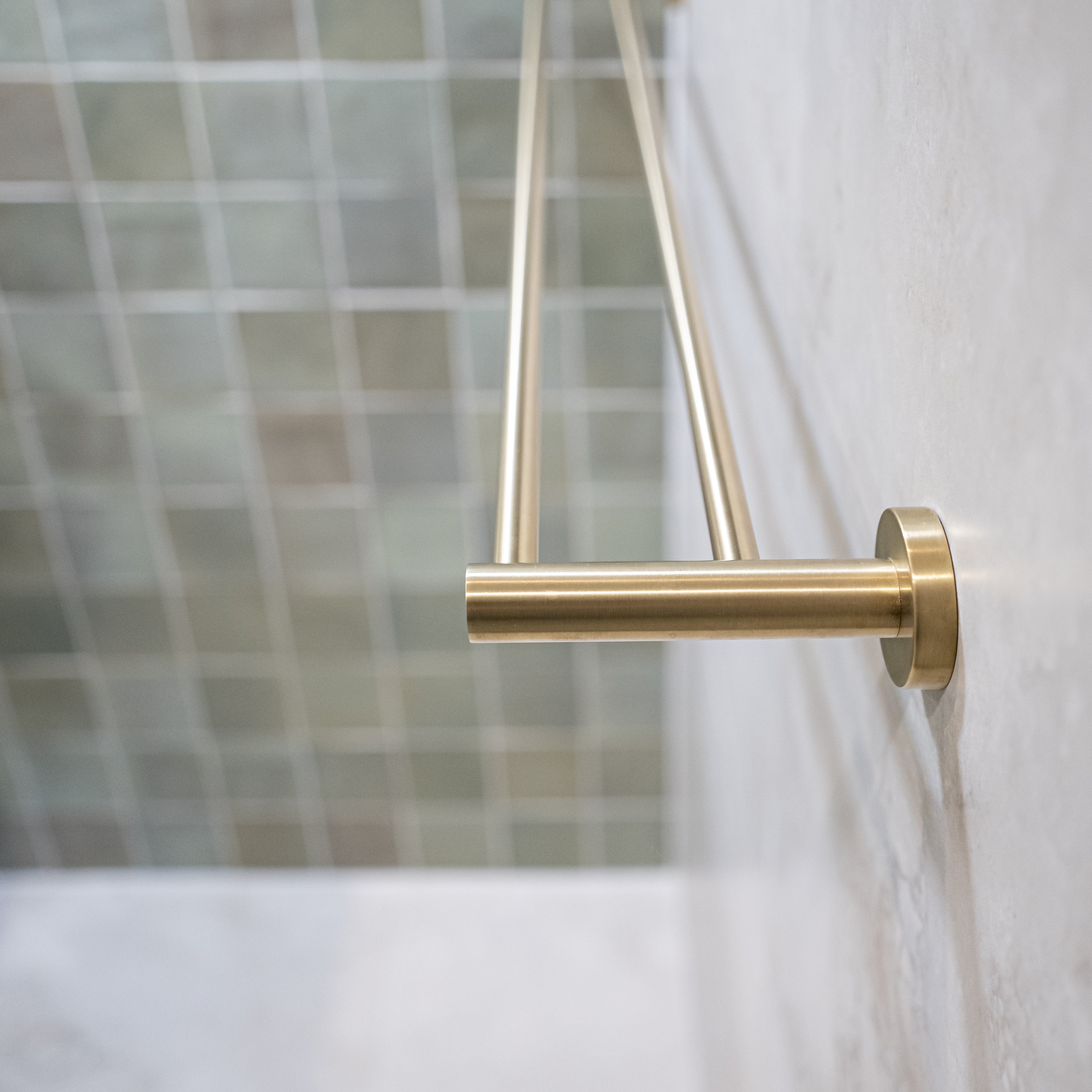 A brushed gold double towel rail wall mounted on a tile wall