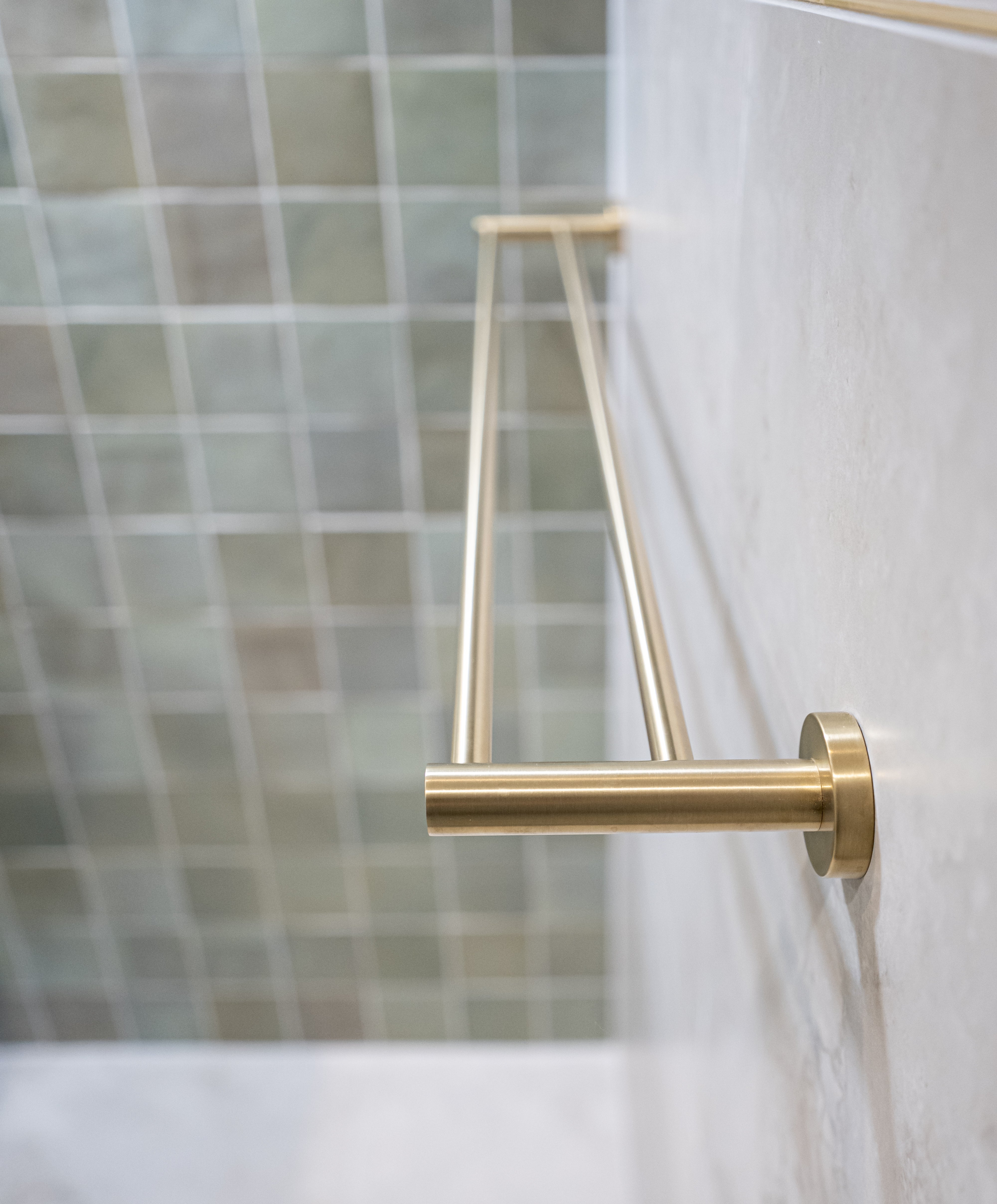 A brushed gold double towel rail wall mounted on a tile wall