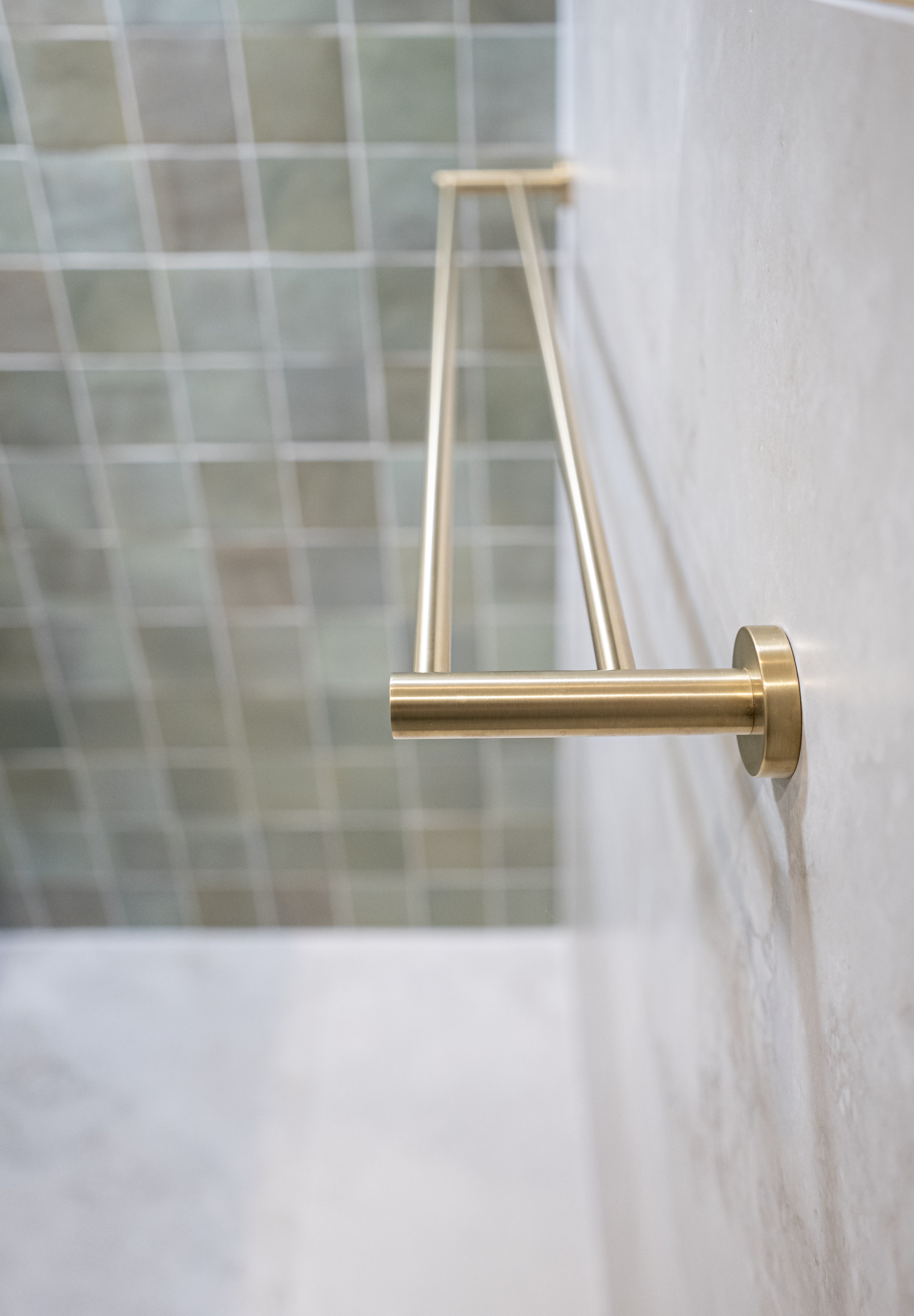 A brushed gold double towel rail wall mounted on a tile wall