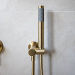a brushed gold handheld shower piece on a wall mounted bracket on a grey background