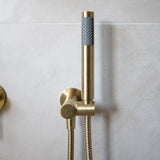a brushed gold handheld shower piece on a wall mounted bracket on a grey background