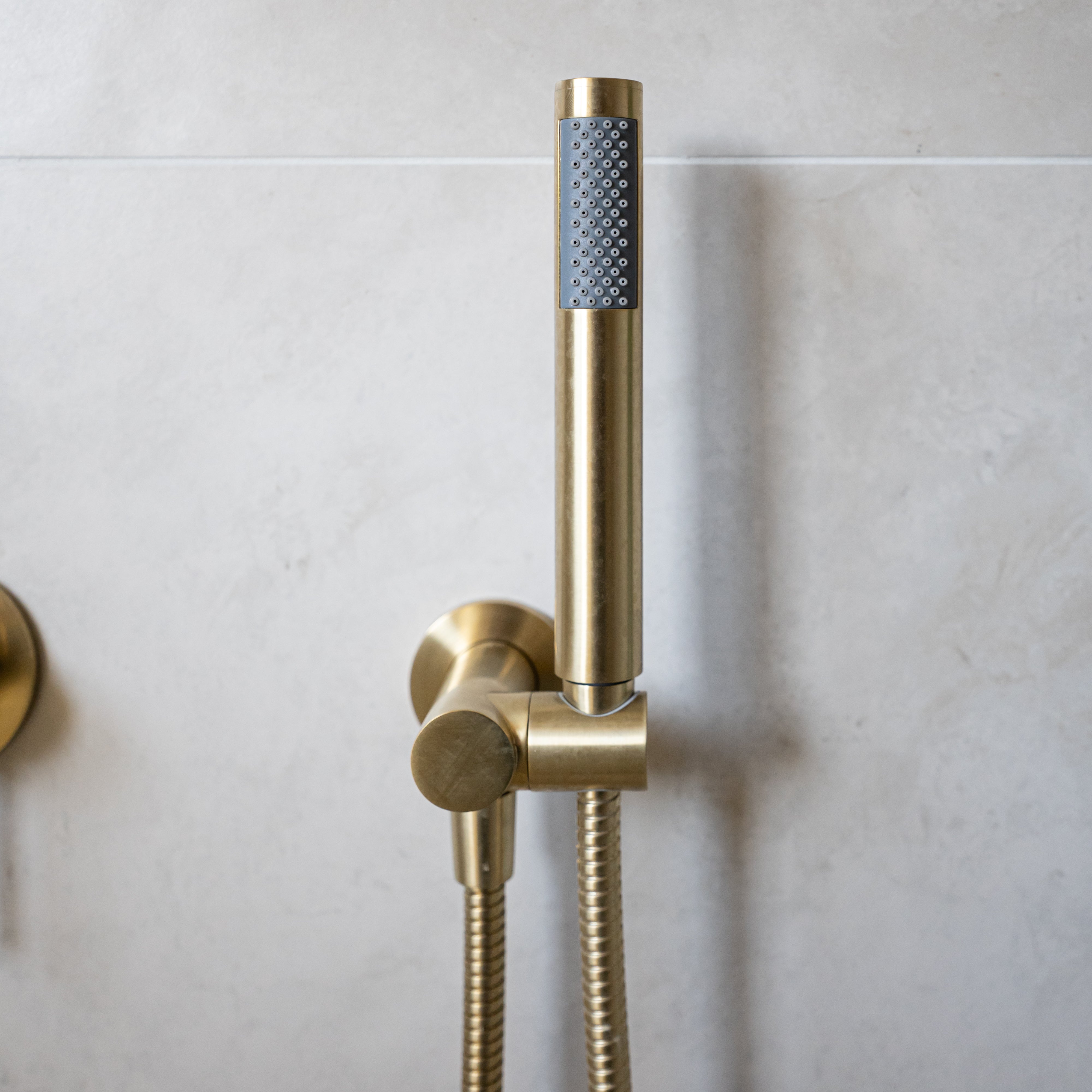 a brushed gold handheld shower piece on a wall mounted bracket on a grey background
