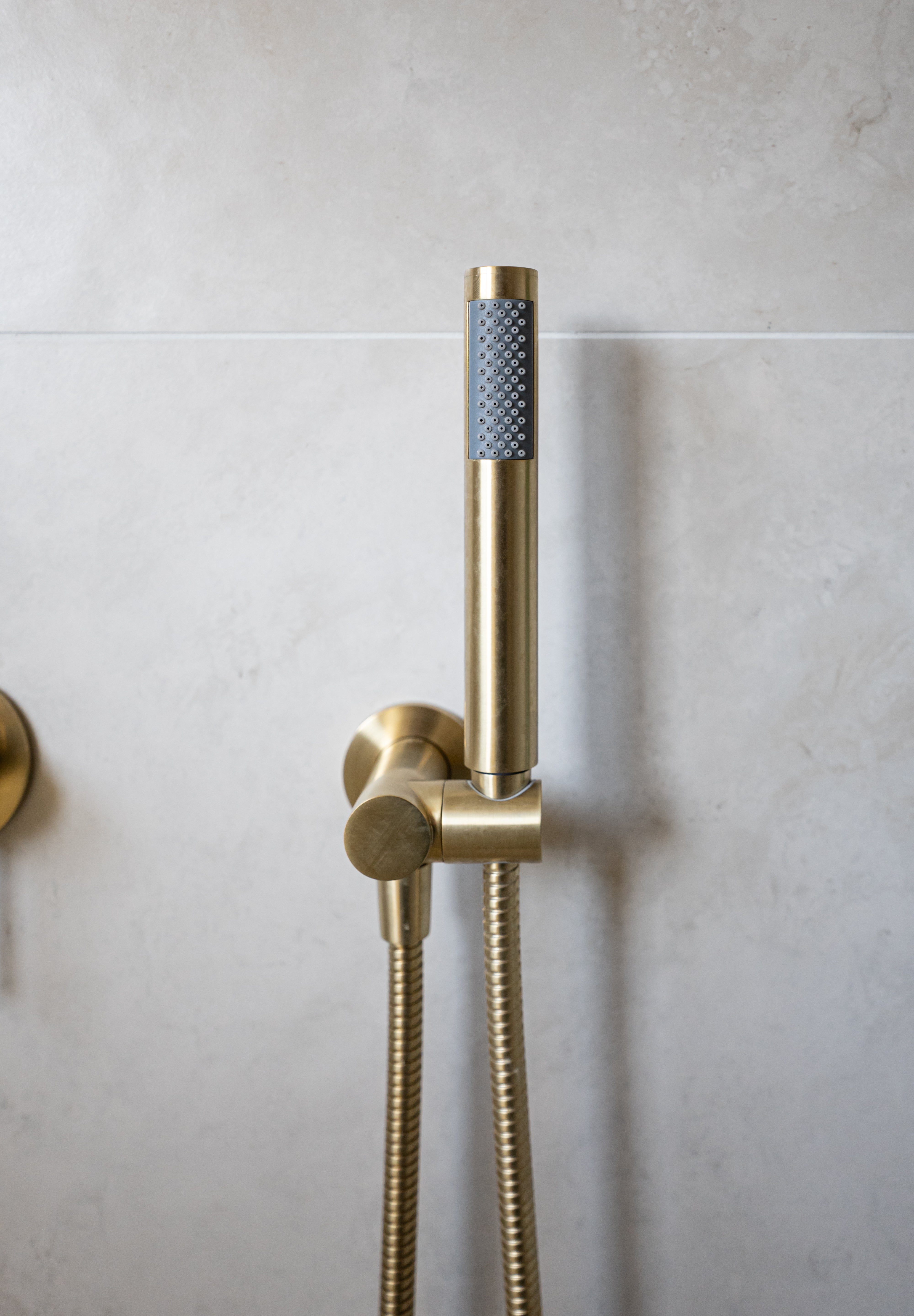 a brushed gold handheld shower piece on a wall mounted bracket on a grey background